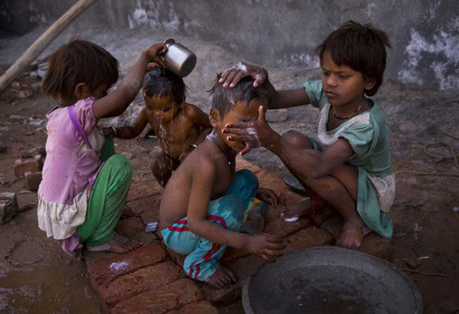 दिल्लीच्या बादशहापूर भागामध्ये रस्त्यावर राहणाऱ्या या मुली आपल्या लहान भावांना आंघोळ घालताना. (छाया- एपी)