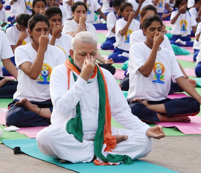 मोदी यांनी तिरंगी पटका व पांढरा पोशाख परिधान केला होता, साधकांना इंग्रजी व हिंदूीतून सूचना दिल्या जात होत्या व आसने मोठय़ा पडद्यावर दाखवली जात होती. (छाया-पीटीआय)