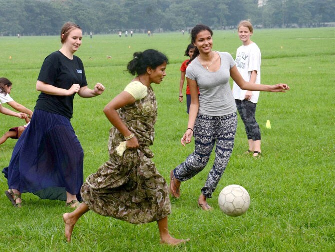 कोलकाता येथील मैदानावर मुलांसह फुटबॉल खेळताना परदेशी स्वयंसेवी संस्थेच्या सदस्या. (छायाः पीटीआय)
