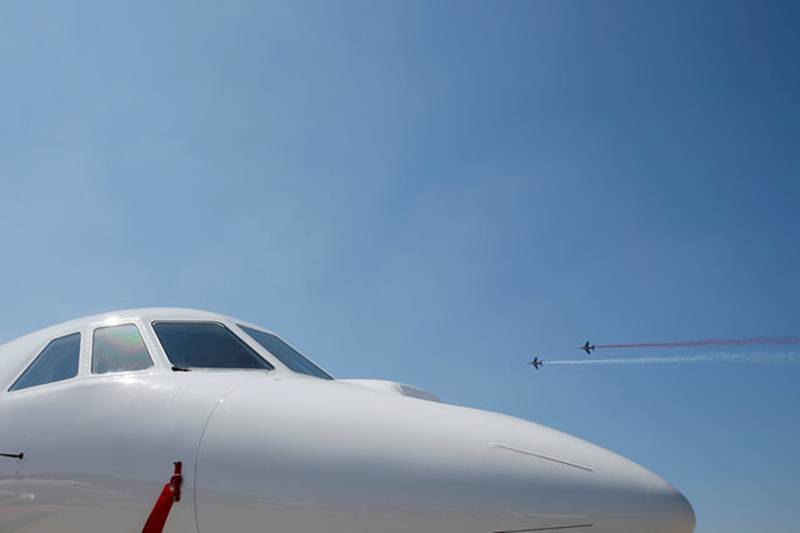 दोन 'Patrouille de France Alphajet' विमानं आकाशात उड्डाण करत आहेत, तर 'Dassault Falcon 2000LXS' जमिनीवर उभे आहे. (रॉयटर्स)