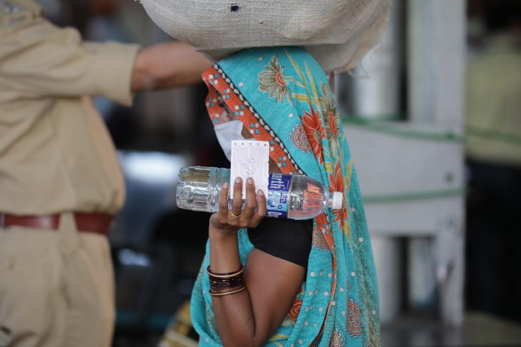 प्रवासासाठीचं तिकीट, पाण्याची बाटली आणि डोक्यावर सामान घेऊन गाडीत बसण्यासाठी वाट पाहणारी महिला