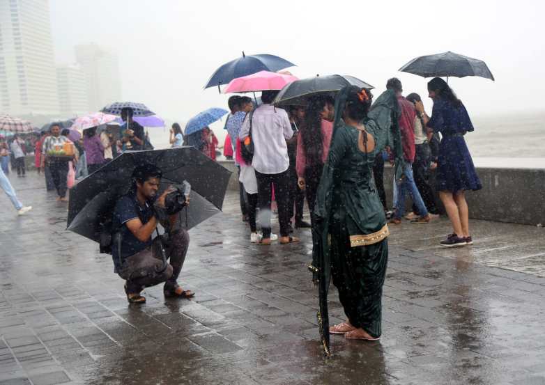 People holding umbrella enjoying amid rains, in Marin Drive, Mumbai