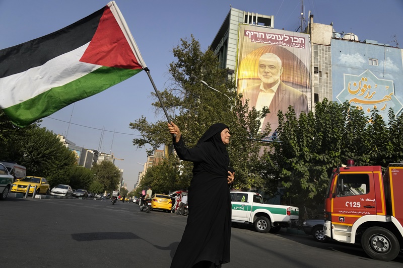 An Iranian woman waves a Palestinian flag prior to start of a demonstration to condemn killing of Hamas leader Ismail Haniyeh, in front of a huge banner on a building showing his portrait with a sign which reads in Farsi and Hebrew: "Wait for severe punishment," at Felestin (Palestine) Sq. in Tehran, Iran, Wednesday, July 31, 2024.