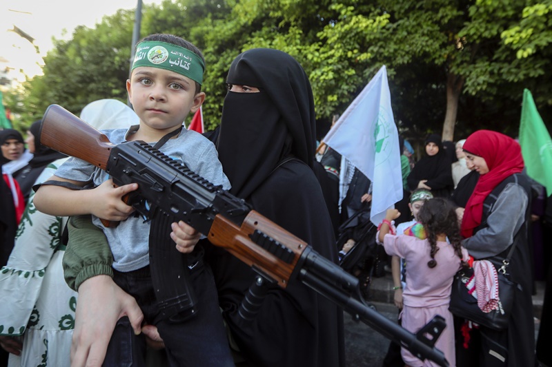 A supporter of the Islamist Hamas movement carries her son, who holds a machine gun toy during a protest in the southern port city of Sidon, Lebanon, Wednesday, July 31, 2024, to condemn the killing of Hamas political chief Ismail Haniyeh.